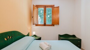 A bedroom with a bed, a nightstand, a dresser, and a window with a view of trees. - Apartment 'Appartamento Con Vista Piscina 2' with Shared Pool, Wi-Fi and Air Conditioning (Castellammare del Golfo)