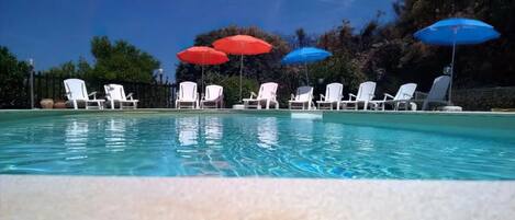 A swimming pool with white lounge chairs and umbrellas.