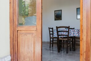 A wooden door leading to a dining area with a table and chairs, a framed picture on the wall, and a tiled floor.