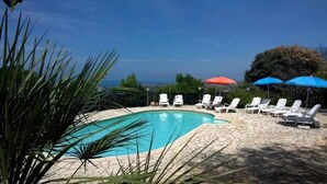 A swimming pool with lounge chairs and umbrellas, surrounded by a stone patio and greenery.