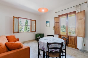 Une pièce comprenant un canapé, une table à manger avec des chaises, un meuble vert et une fenêtre donnant sur des arbres.