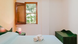 Un dormitorio con cama, una mesita de noche con lámpara, una ventana con vista a árboles y un aparador verde.