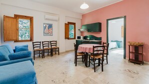 A living room with a sofa, dining table, chairs, and a kitchen area with cabinets and a microwave. - Apartment 'Appartamento Standard 6' with Shared Pool, Wi-Fi and Air Conditioning (Castellammare del Golfo)