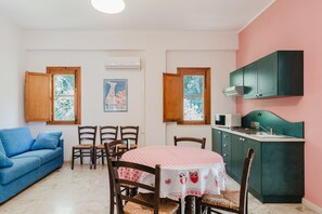 Un espace de vie compact comprenant une table à manger, des chaises, un canapé, un coin cuisine et une fenêtre donnant sur un paysage agréable.