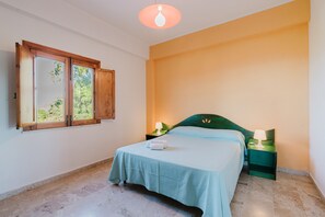 A bedroom with a bed, a nightstand, a lamp, a window with a view, and a ceiling light.