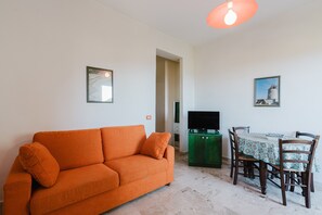 A living room with a sofa, a dining table with chairs, a television, and framed pictures on the wall.