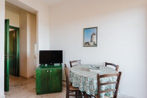 A dining area with a table, chairs, a television on a cabinet, and a painting on the wall.