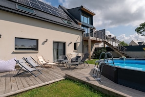 Une maison moderne dotée d’une piscine, de chaises longues et d’un escalier menant à un balcon.