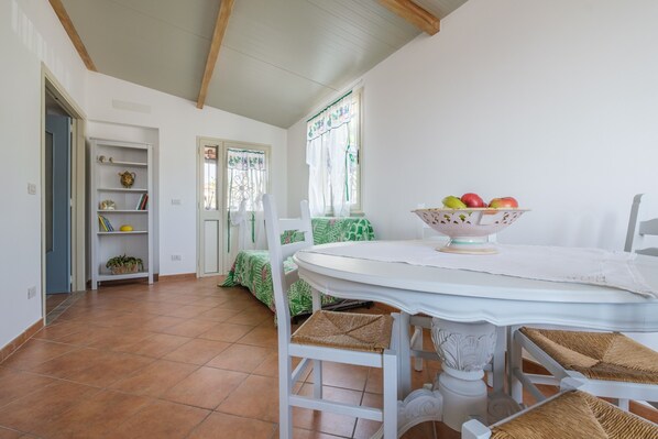 Un coin repas avec une table ronde, des chaises blanches et un saladier rempli de fruits.