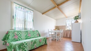 A room with a sofa, a dining table, chairs, a kitchen area, and a window with curtains. - Apartment 'Medusa' with Balcony, Wi-Fi and Air Conditioning (Taormina)
