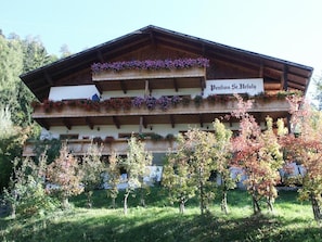 Un chalet traditionnel doté de plusieurs balcons ornés de fleurs, une enseigne indiquant « Penifon St. Ulrula », et entouré d’arbres.