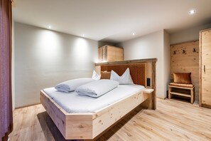 Un lit en bois avec une literie blanche, une table de chevet en bois, une armoire en bois et une petite chaise en bois.