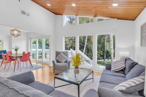 A spacious living area with a glass coffee table, grey sofas, and a dining table with red chairs.
