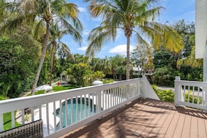 A wooden deck with a white railing, a swimming pool, and palm trees. - Siesta Key Home, Heated Pool, Theater & Arcade (Siesta Key)