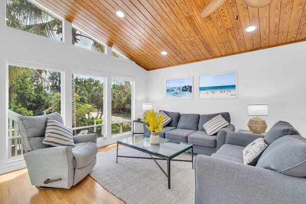 A modern living room with a glass coffee table, grey sofas, and a wooden ceiling.