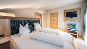 Une chambre d’hôtel moderne avec un grand lit, un téléviseur fixé au mur et une tête de lit en bois.