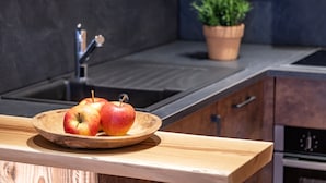Un plan de travail de cuisine avec un saladier en bois rempli de pommes, une plante en pot et un robinet moderne.