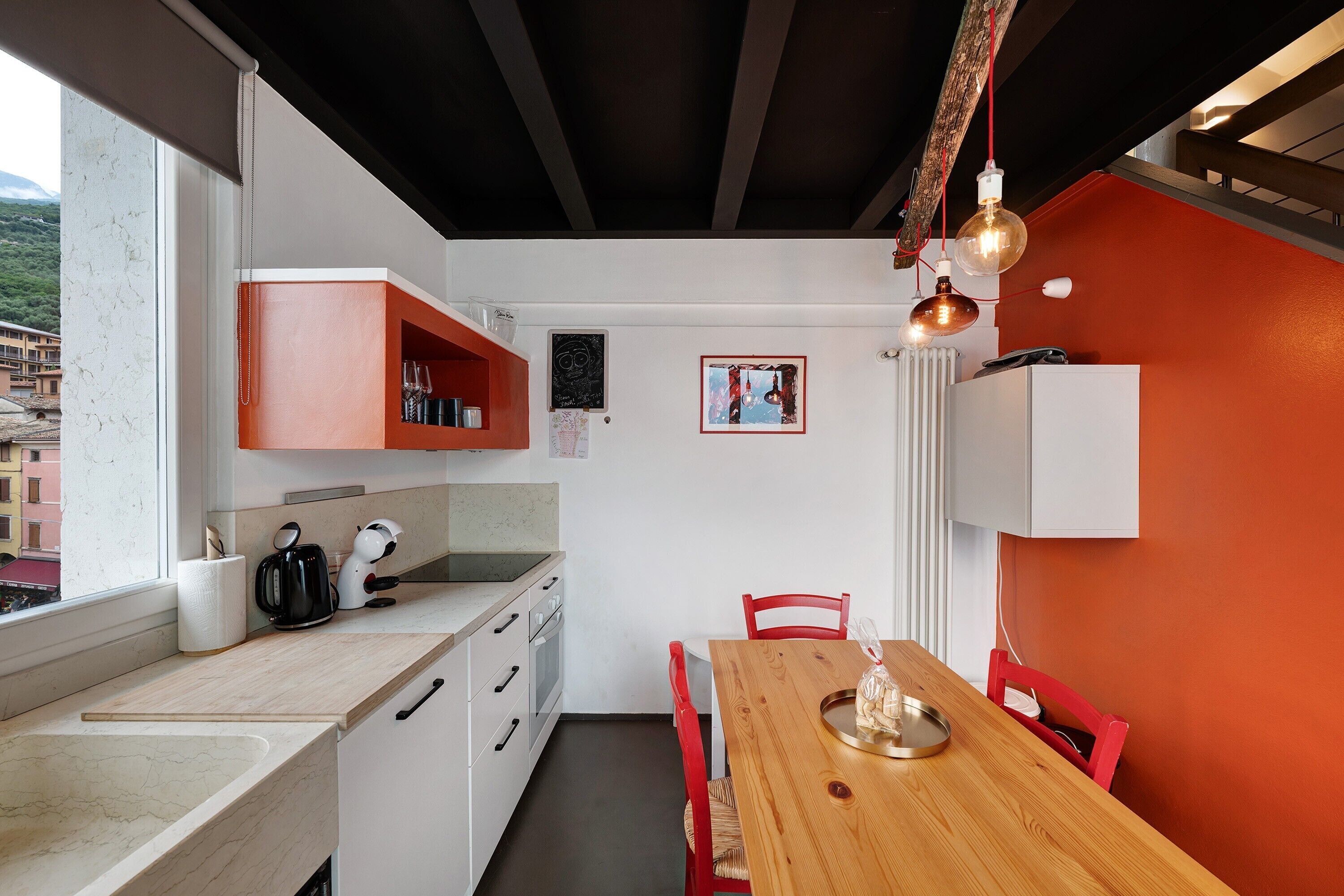 A compact kitchen with white cabinets, a wooden dining table, and red chairs.