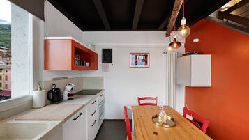A compact kitchen with white cabinets, a wooden dining table, and red chairs.