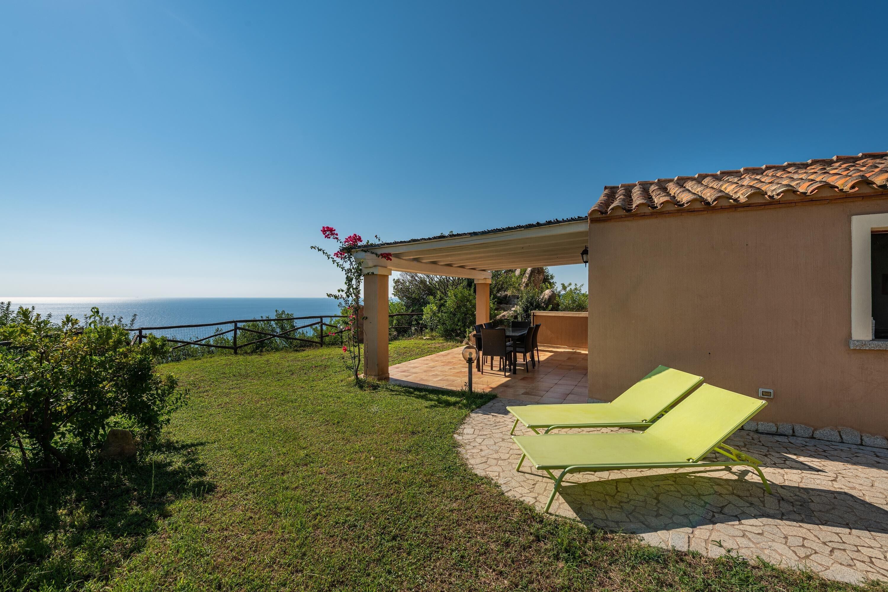 Una casa con un patio, una mesa y dos sillones de jardín verdes.