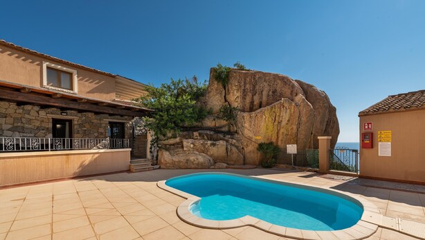 A swimming pool with a stone wall and a view of the sea.