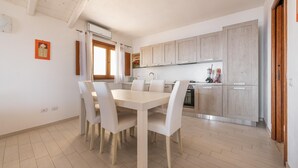A modern kitchen with light wood cabinets, a white dining table with chairs, and a window with curtains.