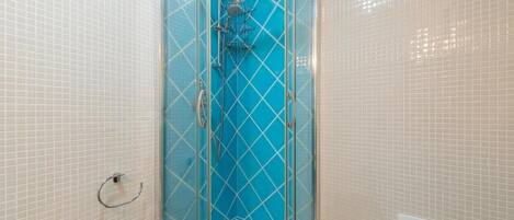 A glass-enclosed shower with a blue-tiled wall, a white sink, and a beige tiled floor.