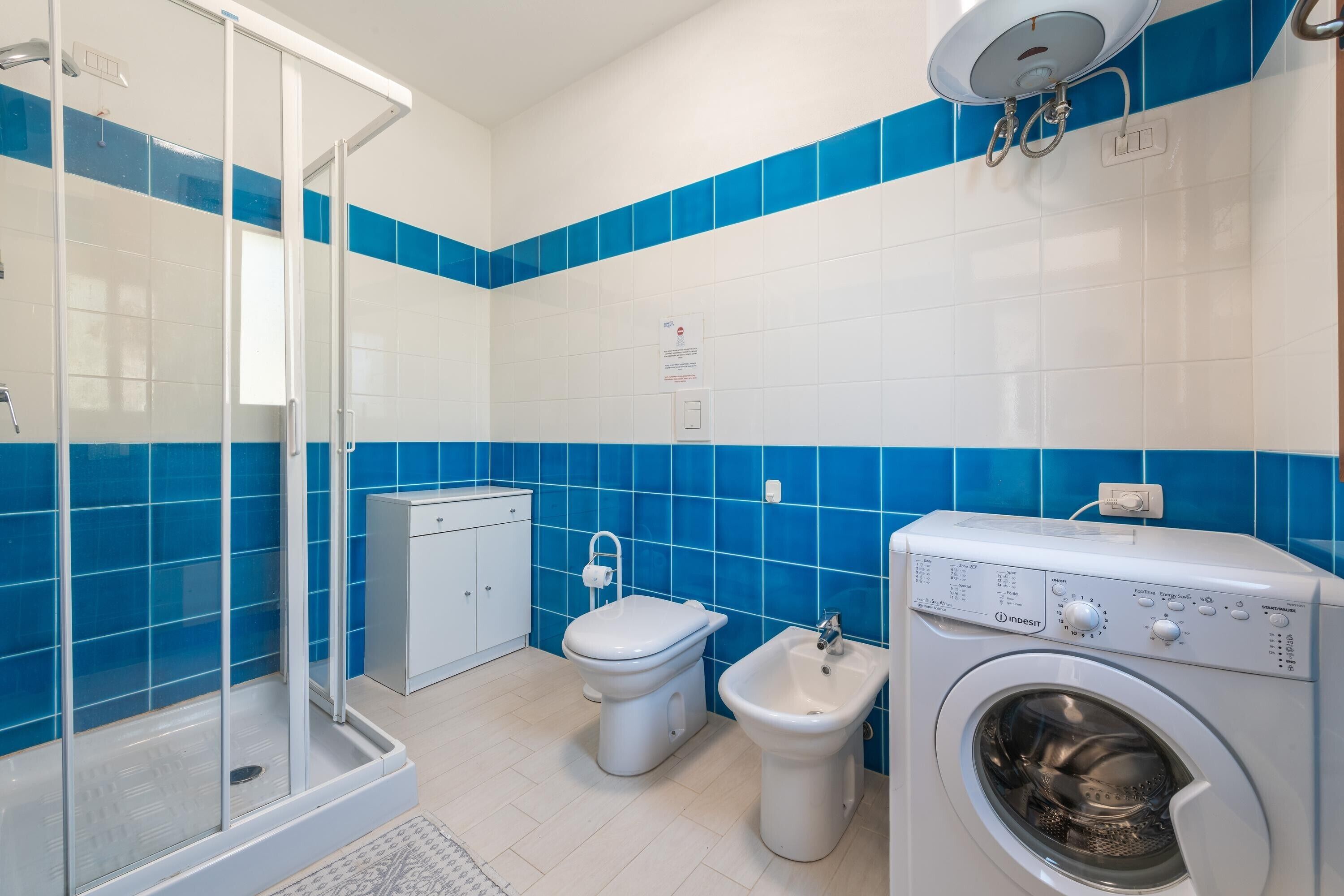 Een badkamer met een douchecabine van glas, toilet, bidet en een voorlader wasmachine.