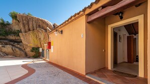A building with a stone-paved entrance, a wooden door, and a view of a rocky cliff.