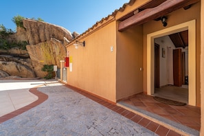 A building with a stone-paved entrance, a wooden door, and a view of a rocky cliff.