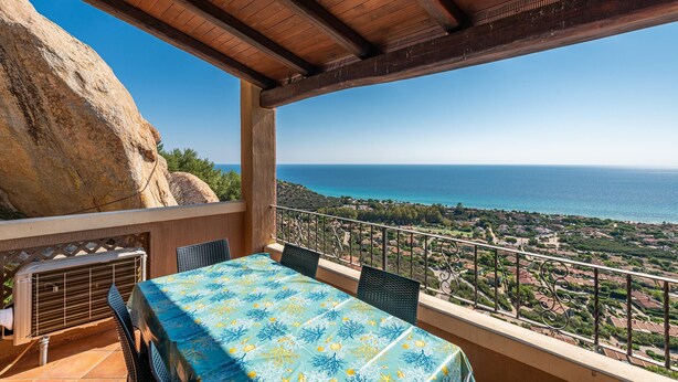 A balcony with a table and chairs, overlooking a coastal landscape.