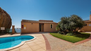A swimming pool, a large rock, a building with a tiled roof, and a well-maintained lawn.