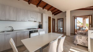 A modern kitchen with white cabinets, a dining table, and chairs. There is a balcony with outdoor furniture.