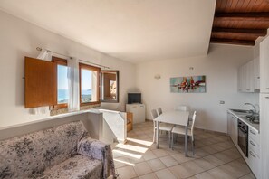 Un ambiente compatto con divano, tavolo da pranzo, TV e angolo cottura.