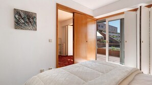 Un dormitorio con una cama, un ventanal corredero que da a un balcón y un cuadro en la pared.