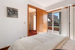 Un dormitorio con una cama, un ventanal corredero que da a un balcón y un cuadro en la pared.