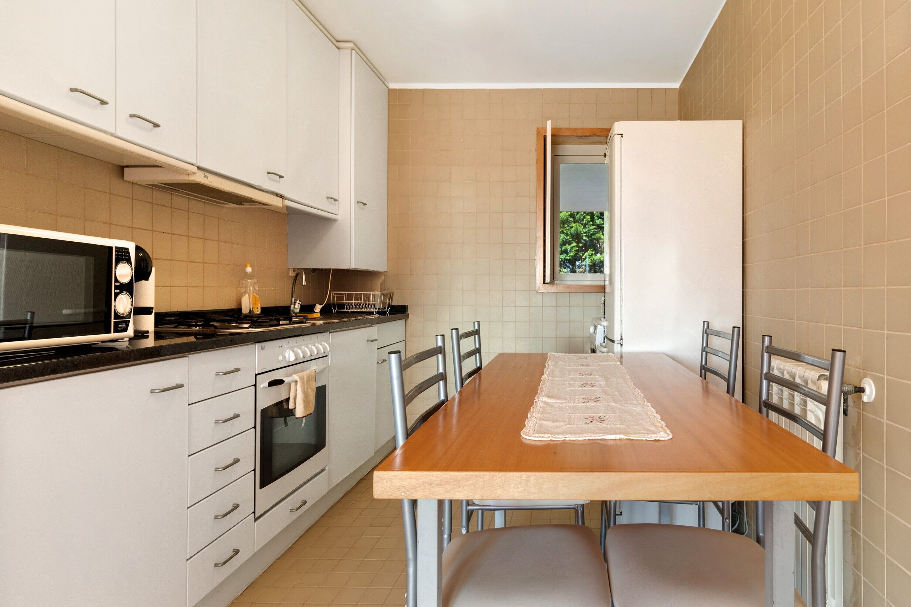 A modern kitchen with white cabinets, a wooden dining table, and a built-in oven.