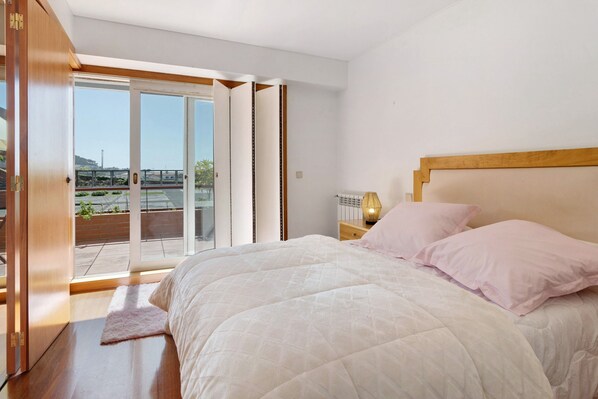 A bedroom with a large bed, a nightstand, a lamp, and a sliding glass door leading to a balcony.
