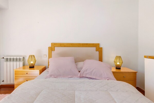 A bedroom with a bed, two bedside tables, a wooden headboard, and a radiator. - Apartment 'Solmar' with Sea View, Balcony and Wi-Fi (Moledo)