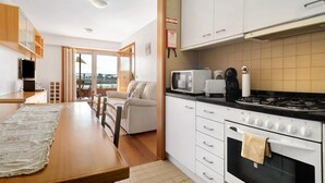 Una cocina con estufa, microondas y armarios, un comedor con mesa y sillas, y vista a través de un ventanal.