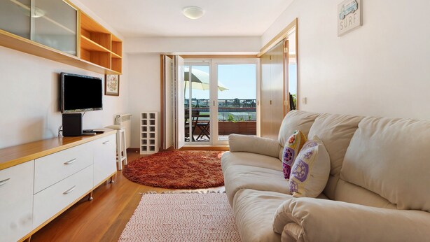 Una sala de estar moderna con un televisor de pantalla plana, un sofá color beige, un mueble de madera y un ventanal con vistas.