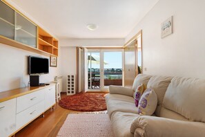 A modern living room with a flat-screen TV, a beige sofa, a wooden cabinet, and a large window with a view. - Apartment 'Solmar' with Sea View, Balcony and Wi-Fi (Moledo)