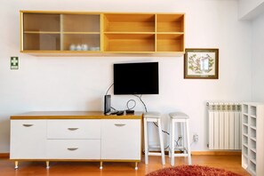 A room with a wooden cabinet, a television, two white stools, a framed picture, and a radiator.