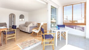 A modern living room with a sofa, chairs, a dining table, and a large window.