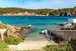 Un paysage côtier avec une eau bleue et limpide, des bateaux, une plage de sable et un terrain rocheux.