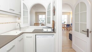 A modern kitchen with white cabinetry, a built-in dishwasher, and a dining area with a table and chairs.