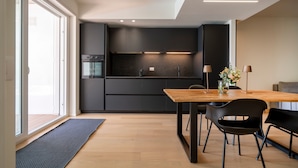 Une cuisine moderne avec des meubles de couleur sombre, un four encastré et un coin repas comprenant une table en bois et des chaises noires.