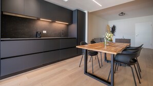 Une cuisine moderne avec des meubles de couleur sombre, une table à manger en bois et des chaises noires.