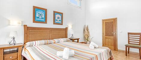 A bedroom with a large bed, wooden headboard, two bedside tables with lamps, a wooden door, and a chair.