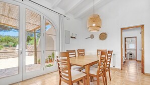 Un comedor con una mesa y sillas de madera, una lámpara de fibra tejida y vistas a un patio exterior a través de puertas de vidrio.